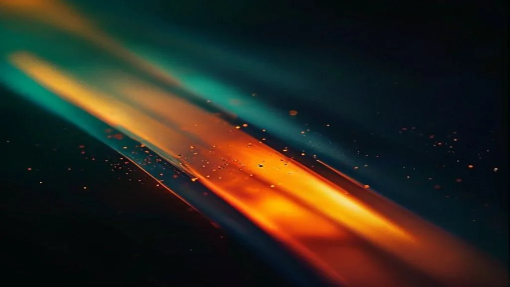 Single thin beam of light grazing a dark matte surface, fragmenting into a narrow ordered band of pale dots